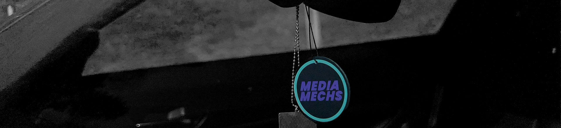 Stilvolle Inszenierung des Media Mechs Brandings: Runder Logo-Anhänger im dunklen, körnigen Fahrzeug-Cockpit – ein visuelles Statement für professionelles Automobil-Marketing